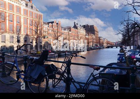 Blick auf den Kloveniersburgwal Kanal in der Altstadt von Amsterdam mit Booten und historischen alten Häusern und blauem Himmel. Stockfoto