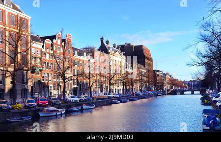 Blick auf den Kloveniersburgwal Kanal in der Altstadt von Amsterdam mit Booten und historischen alten Häusern und blauem Himmel. Stockfoto