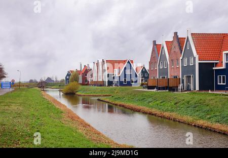 Schöne farbige Häuser am Flussufer mit Brücke und Windmühlen in Volendam, Nordholland, Niederlande. Stockfoto