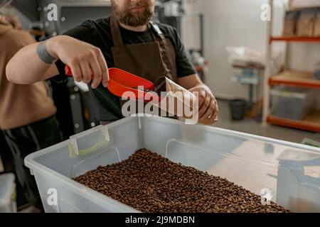 Nahaufnahme eines männlichen Arbeiters in Uniformpackungen geröstete Kaffeebohnen in Verpackungen zum Verkauf Stockfoto