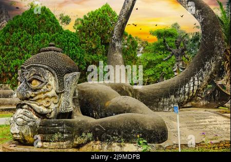 Unheimliche mystische mythologische skulptur aus hinduistischen Steinkrebsen im grünen Garten, spektakulärer Sonnenuntergang am Himmel - Buddha Park (Wat Xieng Khuan), Vientiane, Laos Stockfoto