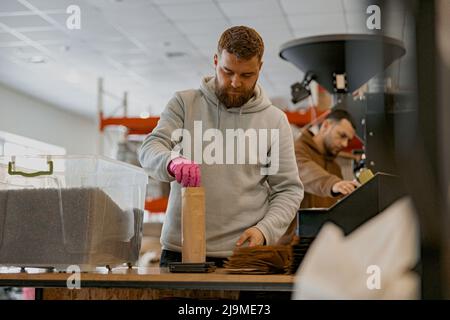 Ein männlicher Arbeiter wiegt in der Kaffeefabrik Papiertüte mit Kaffeebohnen auf einer Waage Stockfoto