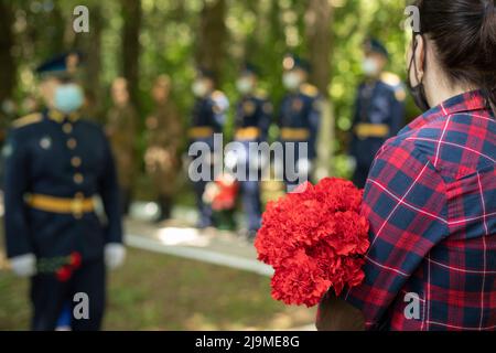 Blumen an der Gedenkstätte. Beerdigung des Soldaten. Mädchen bei der Militärzeremonie. Rote Blumen in den Händen der Frau. Tag des Sieges in Russland. Stockfoto
