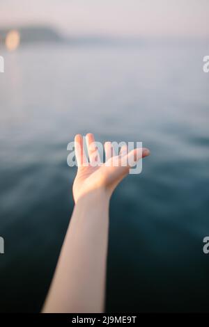 Hoher Erntewinkel nicht erkennbares Weibchen, das bei Sonnenuntergang die Hand gegen das blaue Meer ausstreut Stockfoto