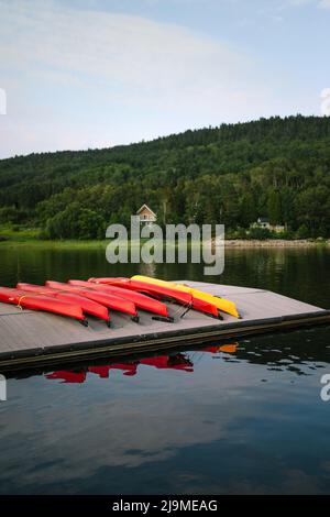 Rote und gelbe Touring Kajaks auf hölzernen Pier in ruhigen Teich Wasser umgeben von Hügeln mit üppigen grünen Bäumen unter bewölktem Himmel platziert Stockfoto