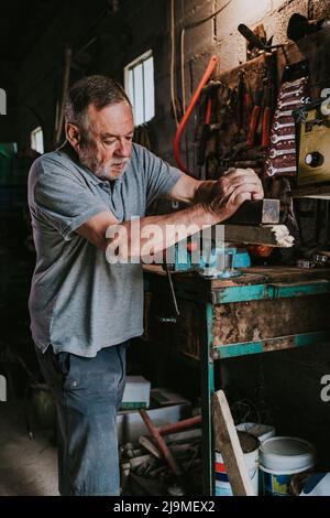 Fokussierter reifer männlicher Holzarbeiter, der Tischler für die Planung von Holzplanken verwendet, während er an einer schäbigen Werkbank in der Schreinerei arbeitet Stockfoto