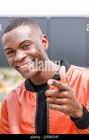 Selbstbewusster junger afroamerikanischer Tausendjähriger Mann in schwarzem T-Shirt und Jeans, der an sonnigen Tagen auf der Straße steht und die Kamera anschaut Stockfoto
