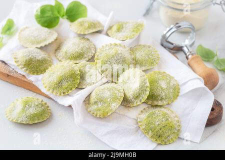 Frische hausgemachte Ravioli mit Basilikumteig auf Serviette auf Holzschneidebrett gelegt Stockfoto