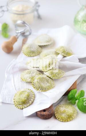 Frische hausgemachte Ravioli mit Basilikumteig auf Serviette auf Holzschneidebrett gelegt Stockfoto