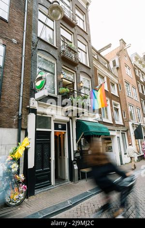 Von unten die LGBT-Regenbogenfahne, die an einem gemauerten Wohnhaus mit Fenstern und geschmiedeten Balkonen in Amsterdam hängt Stockfoto