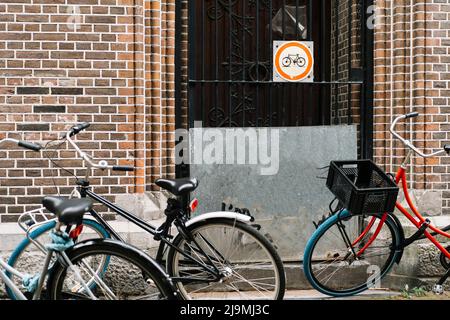 Verschiedene moderne Fahrräder geparkt in der Nähe Zaun des Backsteingebäudes auf der Straße von Amsterdam am Tag Stockfoto