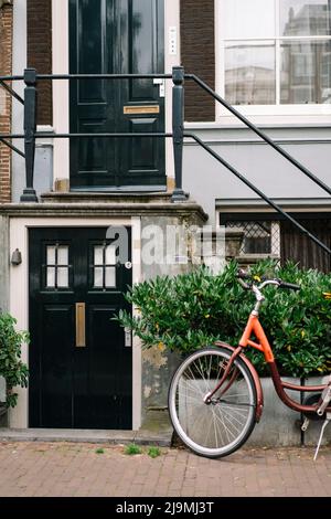 Modernes Fahrrad, das tagsüber in Amsterdam auf der Straße in der Nähe einer Mauer eines modernen Wohngebäudes geparkt wurde Stockfoto