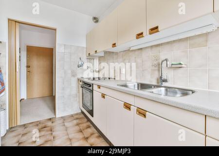 Schränke und verschiedene Utensilien in hellen geräumigen Küche mit Tür und Geschirr in stilvollen Wohnung platziert Stockfoto