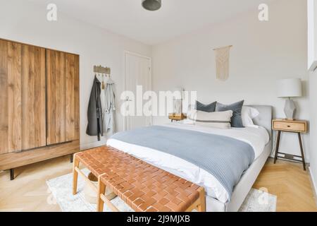 Breites, komfortables Bett mit warmen Decken und weichen Kissen im trendigen Schlafzimmer des modernen Apartments Stockfoto