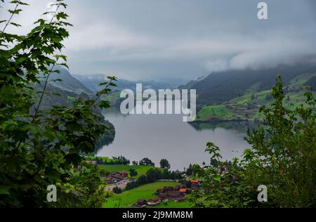 Panoramablick auf die traditionellen Hütten und Häuser im Bergdorf Lungern mit wunderschönen Reflexen auf den Lungersee Stockfoto