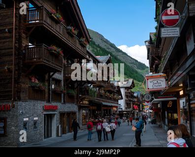 Die malerische Haupteinkaufsstraße von Zermatt mit Restaurants, lokalen Chalet-Häusern, Hotels und Geschäften voller Touristen im Sommer Stockfoto