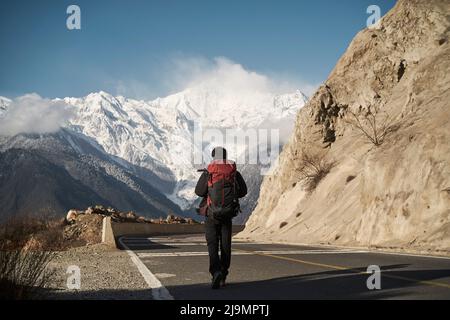 Rückansicht eines asiatischen Wanderers mit Rucksack, der auf der Autobahn mit schneebedeckter meili-Berg im Hintergrund läuft Stockfoto