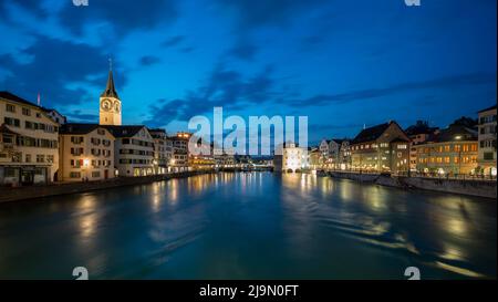 Blick auf die Stadt Zürich von der Münsterbrücke über die Limmat während der Blauen Stunde in Zürich, Schweiz. Stockfoto
