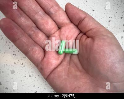 Nahaufnahme von zwei grünen Pillen in der Handfläche einer erwachsenen Hand, vor einem hellen Hintergrund geschossen Stockfoto