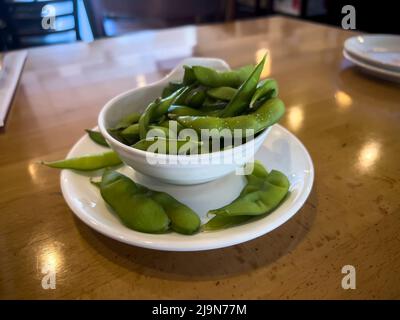 Nahaufnahme, selektiver Fokus auf edamame Schoten in einer kleinen weißen Tasse auf einem Holztisch in einem Restaurant Stockfoto