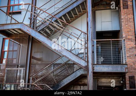 Winkelansicht einer Holztreppe auf der Außenseite eines roten Backsteingebäudes, die zu verschiedenen Ebenen einer Wohnung oder eines Unternehmens führt Stockfoto
