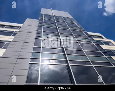 Blick aus der unteren Perspektive auf ein hohes Bürogebäude an einem hellen, sonnigen Tag mit wispigen Wolken Stockfoto