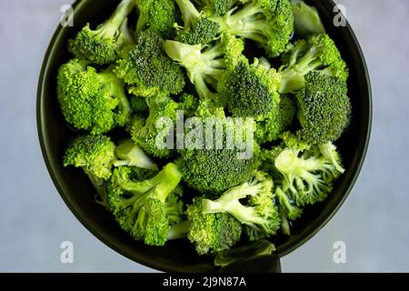 Leuchtend grüne Blütenstände von frischem Brokkoli in einer Bratpfanne in Wasser zum Eintopf. Gesunde Ernährung. Blick von oben. Stockfoto