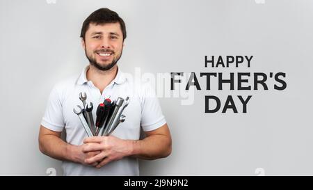 Lächelnder, glücklicher bärtiger Mann mit einem Strauß Schraubenschlüssel, Schraubenschlüsseln und Schraubendrehern mit Inschrift Happy Father's Day. Happy Fathers Day Konzept oder Greeti Stockfoto