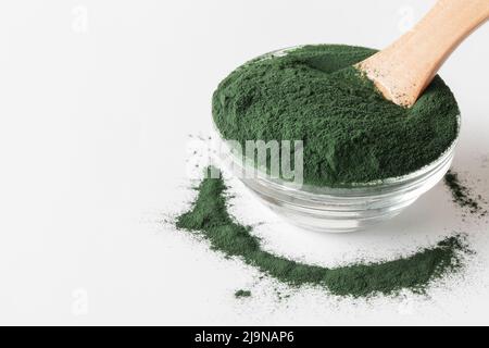 Natürliche Zusatzstoffe und Superfood. Grünes Spirulina Algenpulver im Glas mit Holzlöffel auf weißem Hintergrund. Gesundes Lifestyle-Konzept. Bio-Lebensmittel Stockfoto