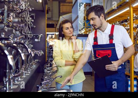 Junge Frau mit langen Haaren, die einen Wasserhahn für Bad oder Küche in einem Einrichtungsgeschäft mit einem Berater wählt. Stockfoto