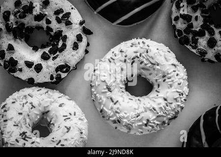 Flaches Lay-Bild von Ringdonut mit weißer Glasur und hunderttausenden anderen Donuts, schwarz-weiß-Bild Stockfoto