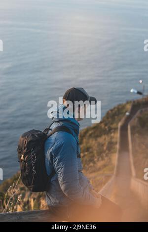 Der Student, der eine Jacke trägt, genießt die Aussicht von Cristo Rei, Camara de Lomos, Madeira, das zu Portugal gehört. Sonnenaufgang an der Atlantikküste. Ermitteln von t Stockfoto