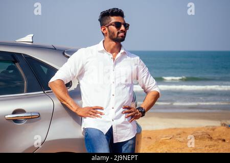 Erfolgreiche junge Geschäftsmann Sonnenbrille am Strand. Afro-Mann, der sich auf seinem Auto vor dem Meer auf der Straße geparkt hat, genießt Ruhe und Stille Stockfoto