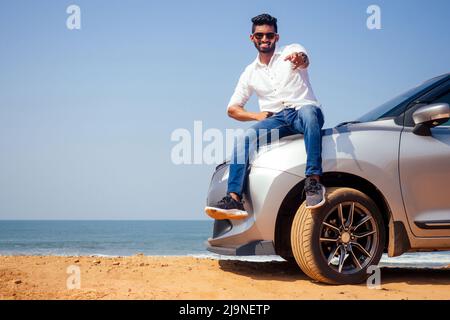 Indischer Geschäftsmann steht in der Nähe von Auto im Freien am Meeresstrand Sommer Guten Tag.ein Mann in einem weißen Hemd und schneeweißem Lächeln freut sich, ein neues Auto zu kaufen Stockfoto