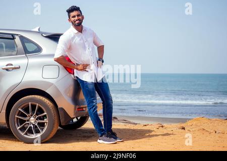 Reiseurlaub glücklicher indischer Mann im weißen Hemdkragen, der ein neues Auto kauft und den Schlüssel zeigt, sitzt im Auto am Strand, Indien octan Goa Stockfoto