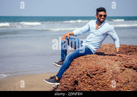 Junger afroamerikanischer Mann in blauem Hemd und Jeans am Meeresstrand. Stockfoto