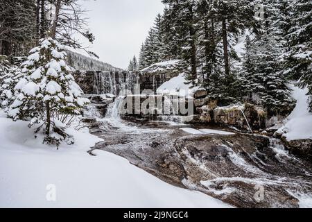 Winterwasserfall namens Certova strouha in Riesengebirge, Tschechische Republik. Verschneite gefrorene Landschaft. Gefrorener Wasserfall und Wildbach, lange Exposition wat Stockfoto