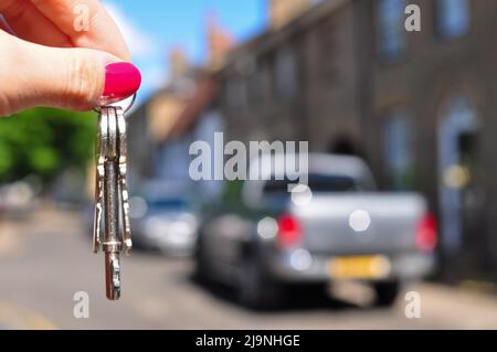 Frauenhand mit Metallschlüsseln auf verschwommenem Hintergrund mit Haus Stockfoto