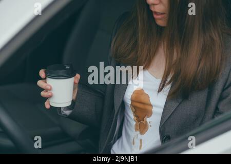 Frau verschüttete heißen Kaffee auf sich selbst während der Fahrt. Konzept der Reinigung Flecken auf Kleidung Stockfoto