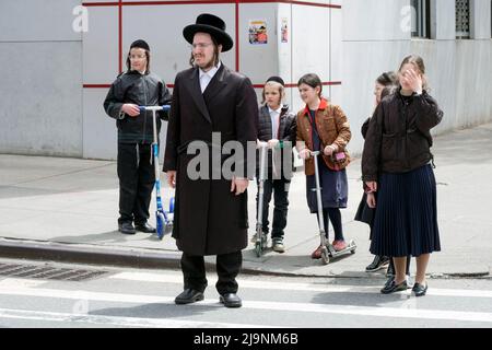 Ein chassidischer Mann und mehrere Kinder - möglicherweise seine Familie - warten darauf, die Straße auf der Bedford Avenue in Williamsburg, Brooklyn, New York City, zu überqueren. Stockfoto