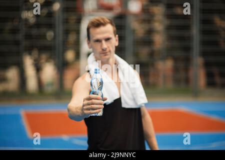 Feuchtigkeitsspendend. Junger Mann in Sportkleidung trinkt Wasser, während er draußen steht. Müder Mann, der sich nach dem Training ausruhte und eine Flasche Wasser in der Hand hielt. Outdoor-Training in der Stadt. Stockfoto