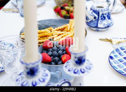 Waffeln mit Beeren auf dem festlichen Sommerwochenende-Tisch im blauen Stil Stockfoto