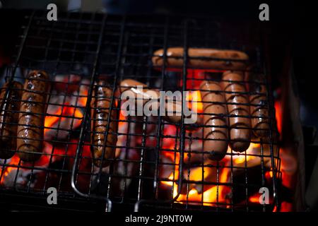 Würste werden über Feuer geröstet. Barbecue am Abend auf der Straße. Fleisch auf offener Flamme kochen. Das Essen zum Abendessen aufwärmen. Saftige Würste mit Cru bedeckt Stockfoto