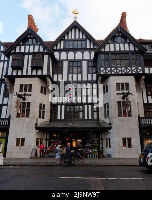 London, Greater London, England, Mai 11 2022: Fahrradfahrer mit orangefarbenem Helm vor dem Liberty-Designer-Apartmentgeschäft Stockfoto