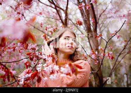 Schöne Frau, die unter einem rosa Blütenbaum im Frühlingspark steht Stockfoto