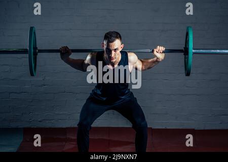 Ein junger Mann macht Übungen mit einer schweren Langhantel im Fitnessstudio Stockfoto