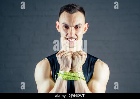 Ein junger Mann mißt seine Hand mit einem Maßband in der Turnhalle auf dunklem Hintergrund Stockfoto