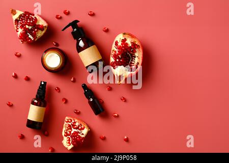 Natürliche Granatapfel-Kosmetik auf rotem Hintergrund. Bernsteinglasflaschen mit Granatapfel- und Samenscheiben. Flach liegend, Draufsicht. Stockfoto