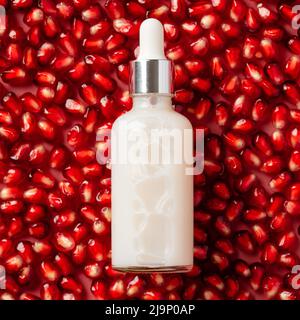 Weißes Serum in Tropfflasche auf Granatapfelkernen Hintergrund. Natürliches Design von Fruchtkosmetik. Stockfoto