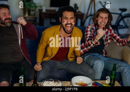 Fröhliche deutsche Fußballfans, Freunde, die Fußball zu Hause anschauen und Popcorn essen. Stockfoto